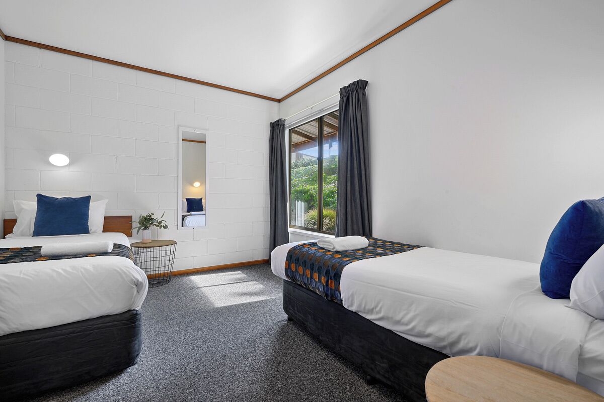 Habitación de hotel con dos camas, una mesita y un ventanal con cortinas.