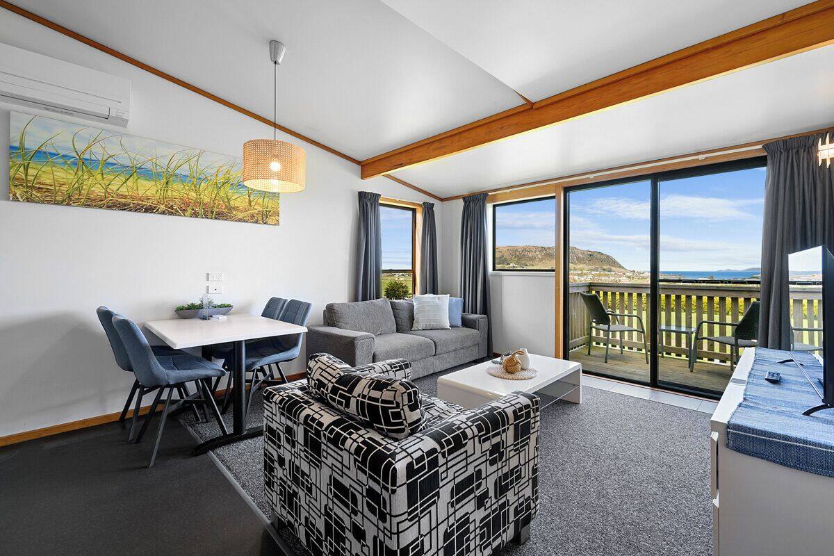 A modern living room with a dining area, large windows, and a balcony with a view.