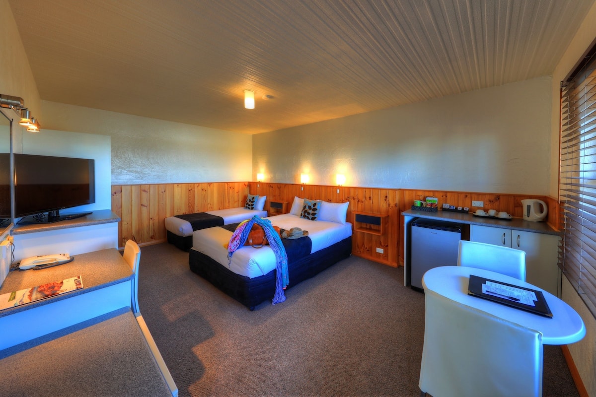 A hotel room with a bed, a desk, a television, and a kitchenette.