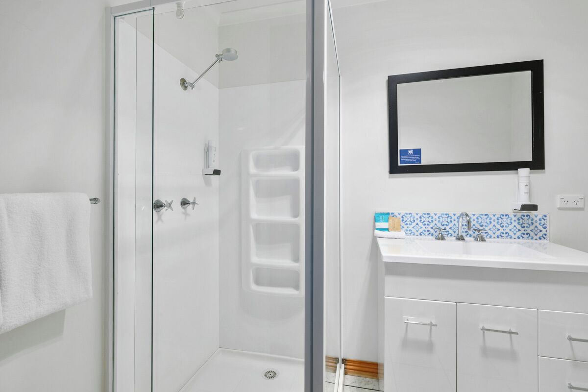 Ein modernes Badezimmer mit einer ein Glasfachwerk-Duschkabine, einem weißen Waschbecken und einem Spiegel mit schwarzem Rahmen, sowie einer gefliesten Spritzschutzwand.