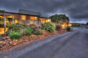 A wooden house with a stone wall and flowering plants in front.
