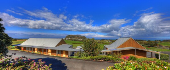 A modern building with a sloped roof, surrounded by lush gardens and a view of a distant hill.