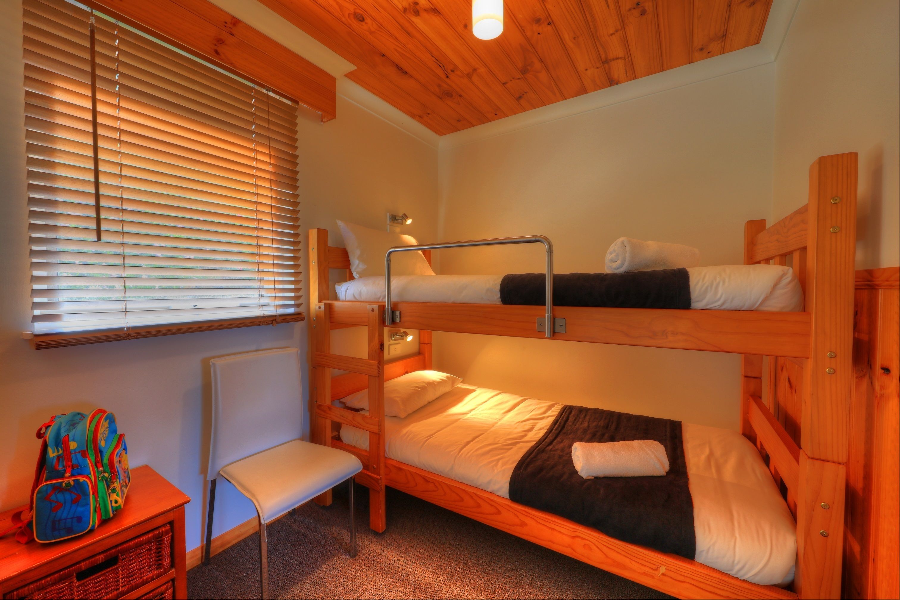 Une chambre avec un lit superposé, une fenêtre, une chaise et une petite table sur laquelle se trouve un sac à dos.