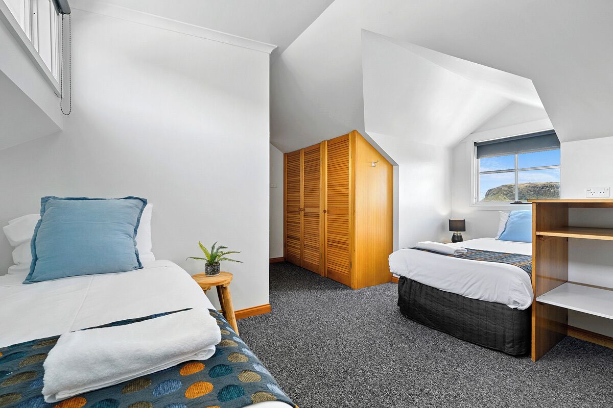 Quarto de hotel moderno com uma cama grande, uma cama menor, um guarda-roupa de madeira, uma escrivaninha e uma janela com vista.