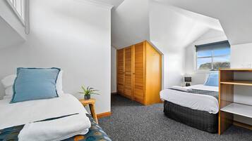 Quarto de hotel moderno com uma cama grande, uma cama menor, um guarda-roupa de madeira, uma escrivaninha e uma janela com vista.