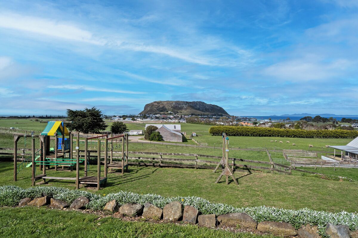 A playground with a slide and climbing structures, a fenced area with sheep, and a hill in the background.