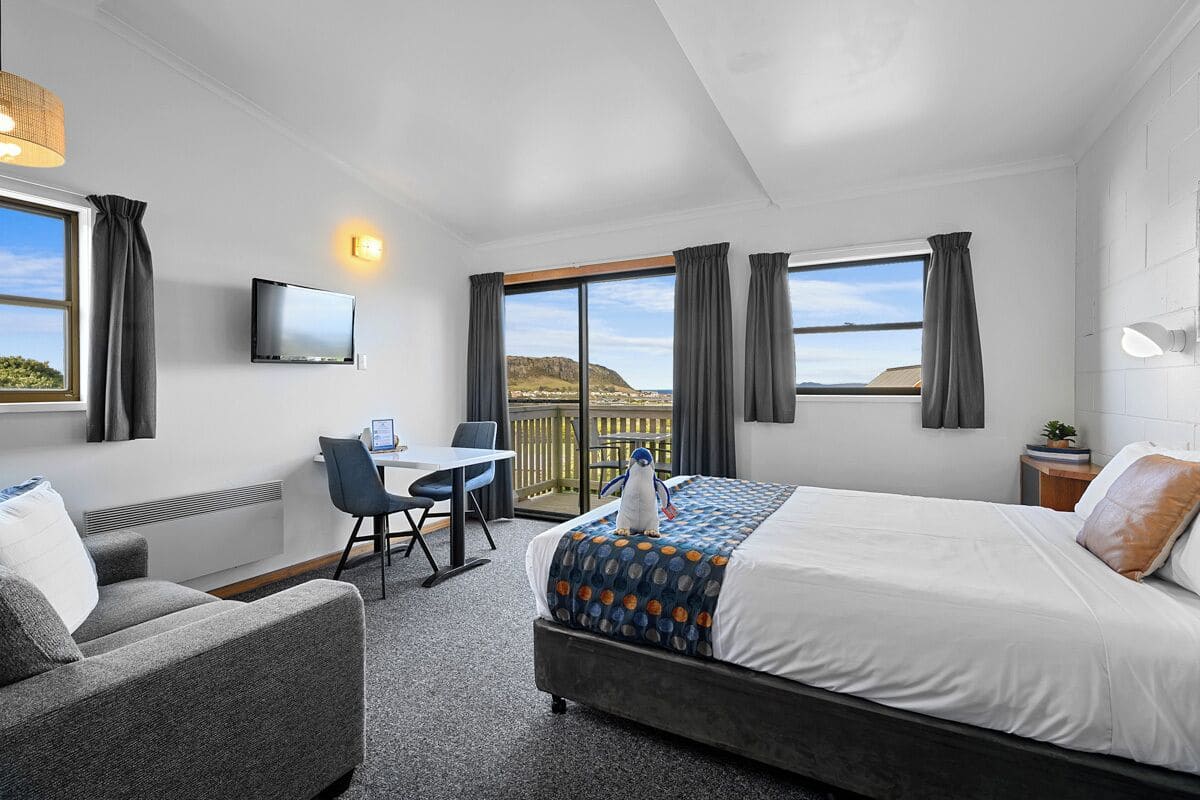 A hotel room with a bed, a desk, a chair, a TV, and a view of the outdoors.