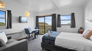 A hotel room with a bed, a desk, a chair, a TV, and a view of the outdoors.