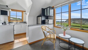 Una cocina moderna con vistas a un paisaje verde, una silla de mimbre y una mesita con un jarrón.