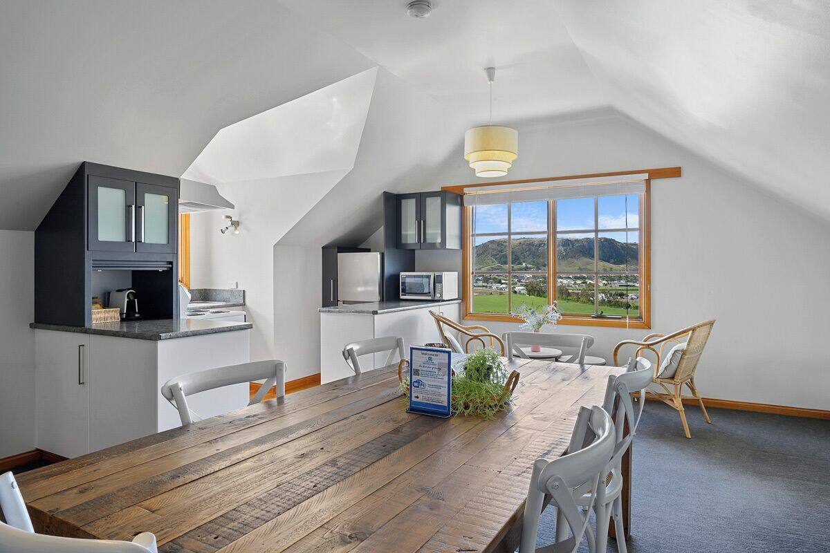 A modern kitchen with a dining area, a view of the countryside, and a sloped ceiling.