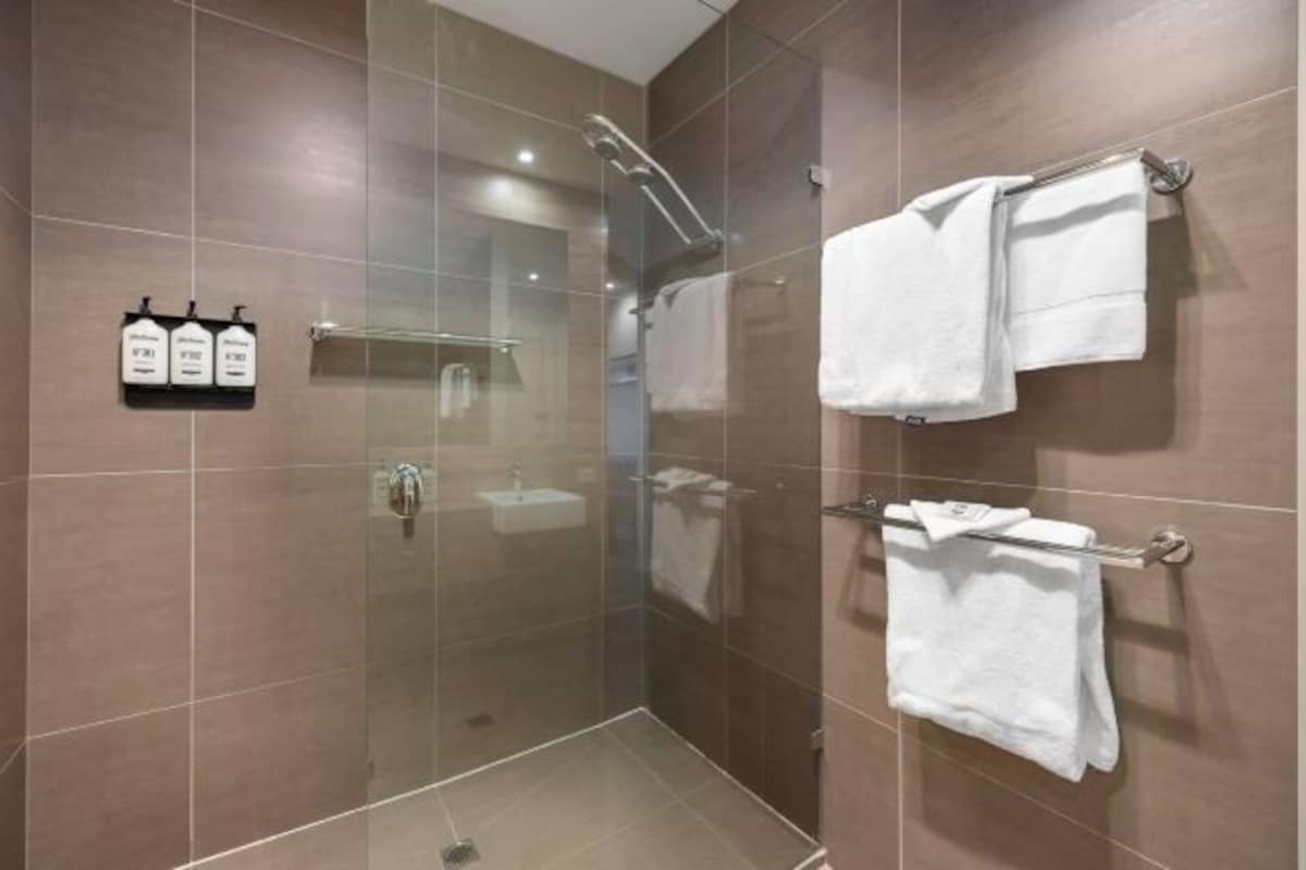 Un baño moderno con ducha envuelta en vidrio, un lavamanos y toalleros.