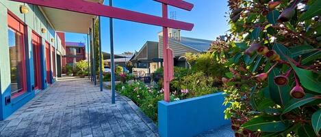 Un pasillo exterior cubierto con una maceta azul, un árbol con hojas verdes y flores rojas.
