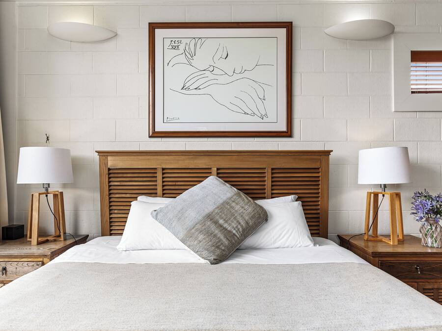 A neatly arranged hotel room with a large bed, two bedside tables with lamps, a framed artwork on the wall, and a window with blinds.