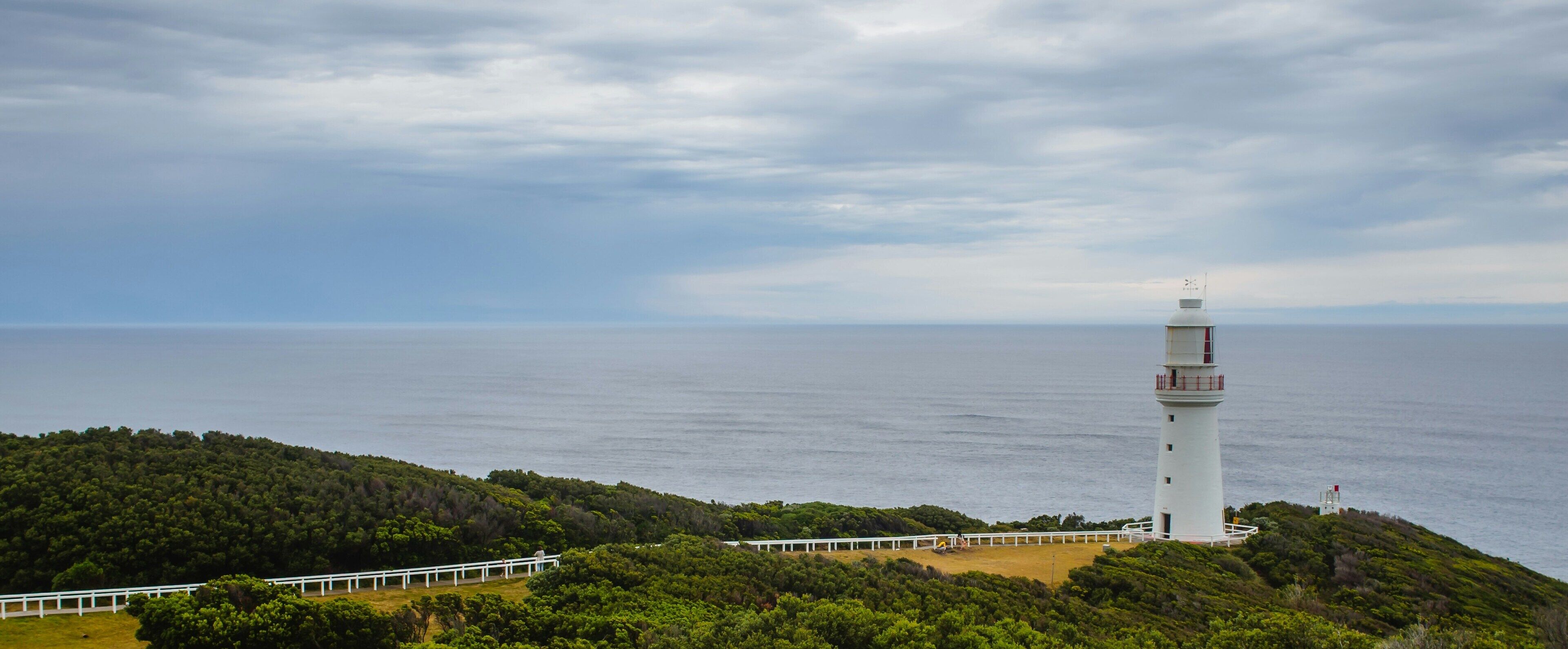 A lighthouse on a hill overlooking the sea, surrounded by greenery.