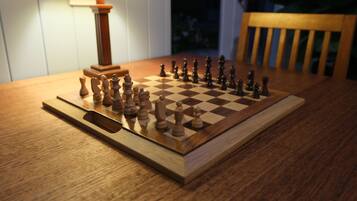 A wooden chessboard on a table with a lamp in the background.