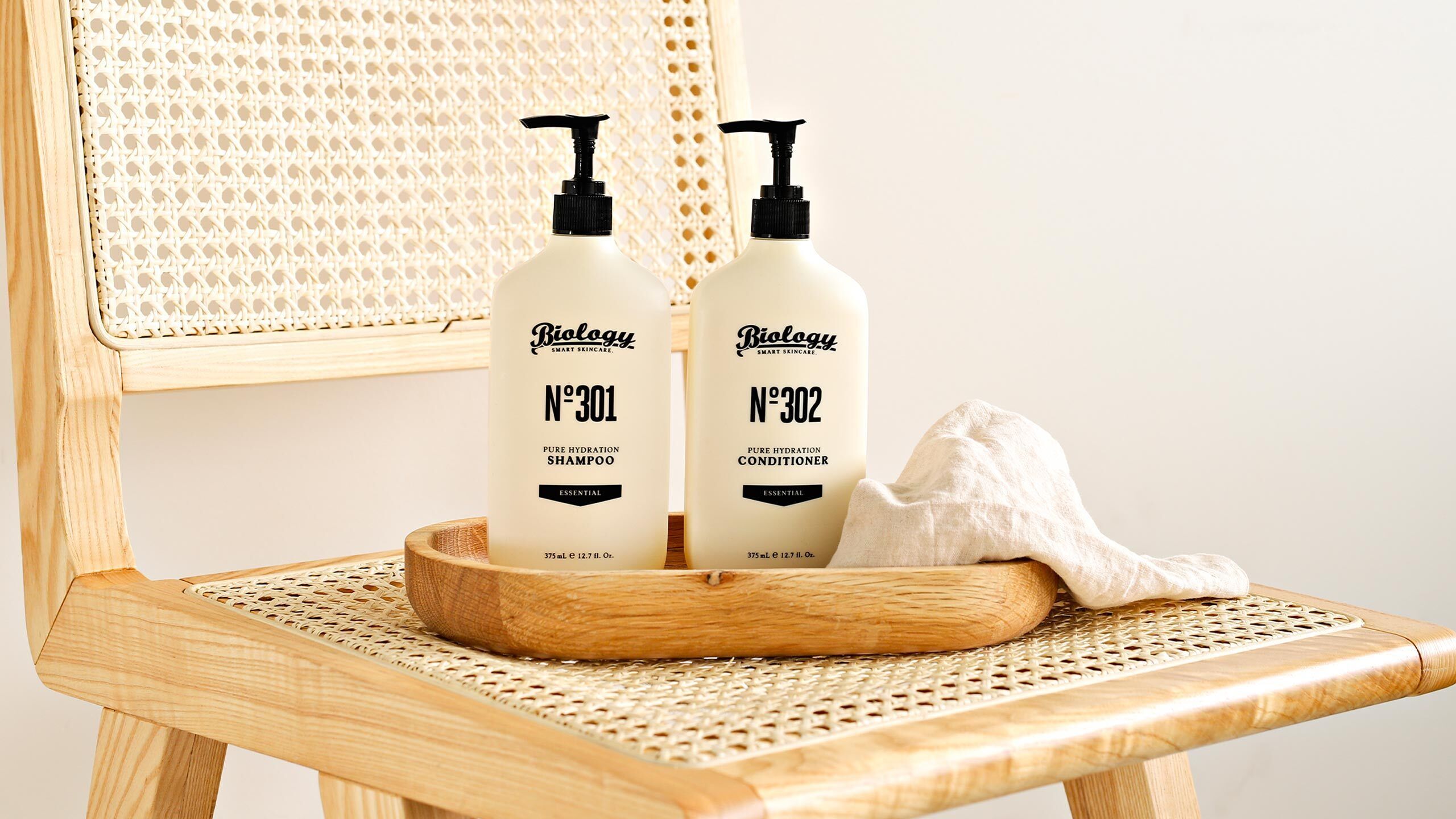 Two bottles of Biolgy Essential products, a wooden chair, and a woven mat.
