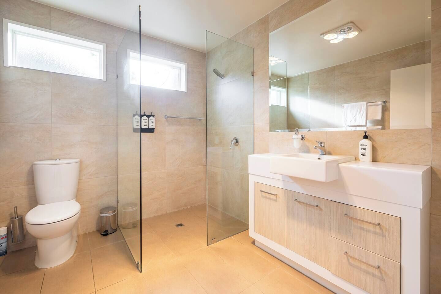 A modern bathroom with a glass-enclosed shower, a toilet, a sink with a mirror, and a cabinet.