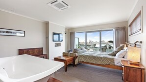 Un dormitorio moderno con una bañera grande, una cama con vistas a la ciudad y un escritorio con lámpara.