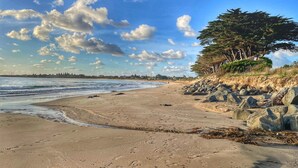 Una playa con costa rocosa, una duna cubierta de vegetación y un cielo despejado con nubes.