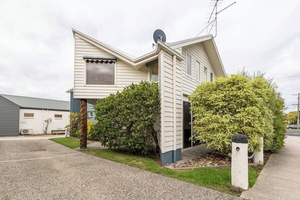 A single-story house with a sloped roof, a satellite dish, and a small front yard with two bushes. - Captains At The Bay (Apollo Bay)