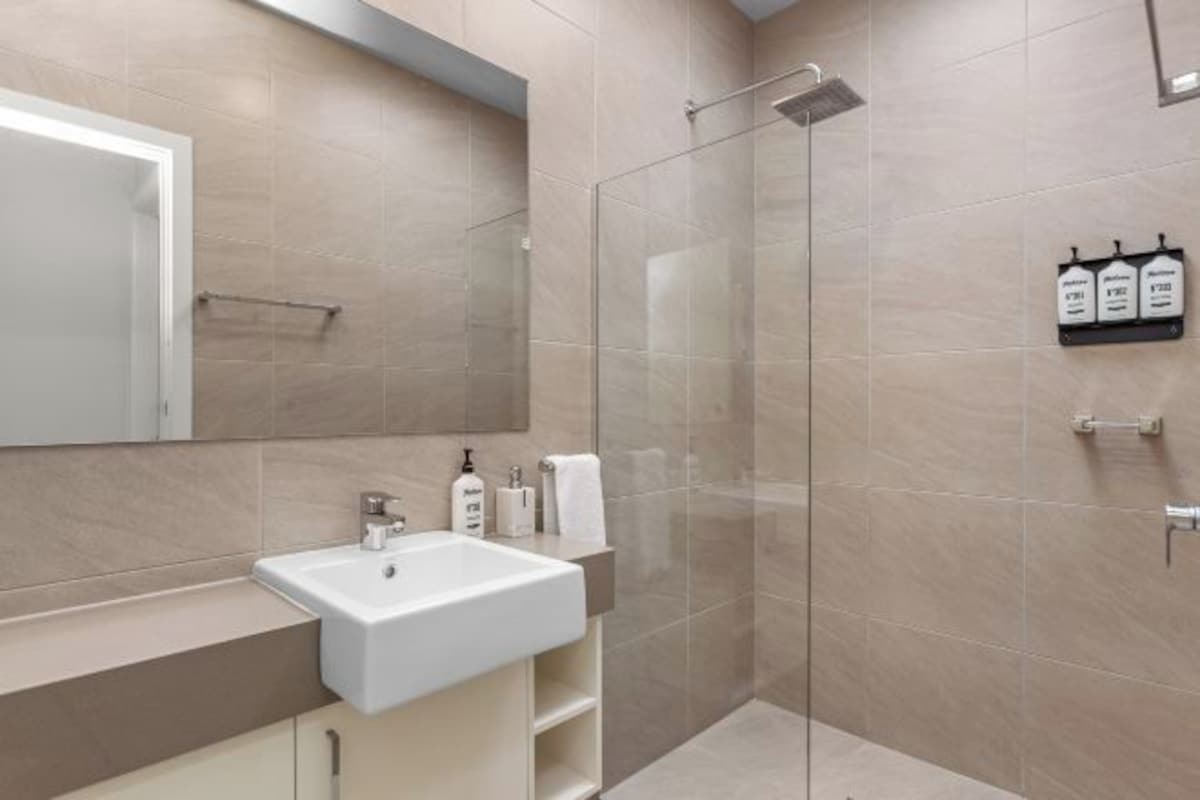 Un baño moderno con cabina de ducha de vidrio, un lavabo blanco y un espejo grande.