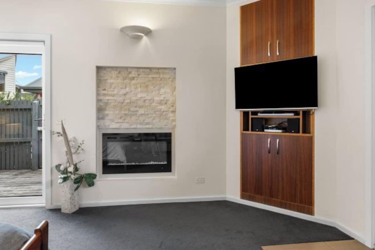 Una habitación con chimenea, televisor montado en un mueble de madera y ventana con pared de piedra.