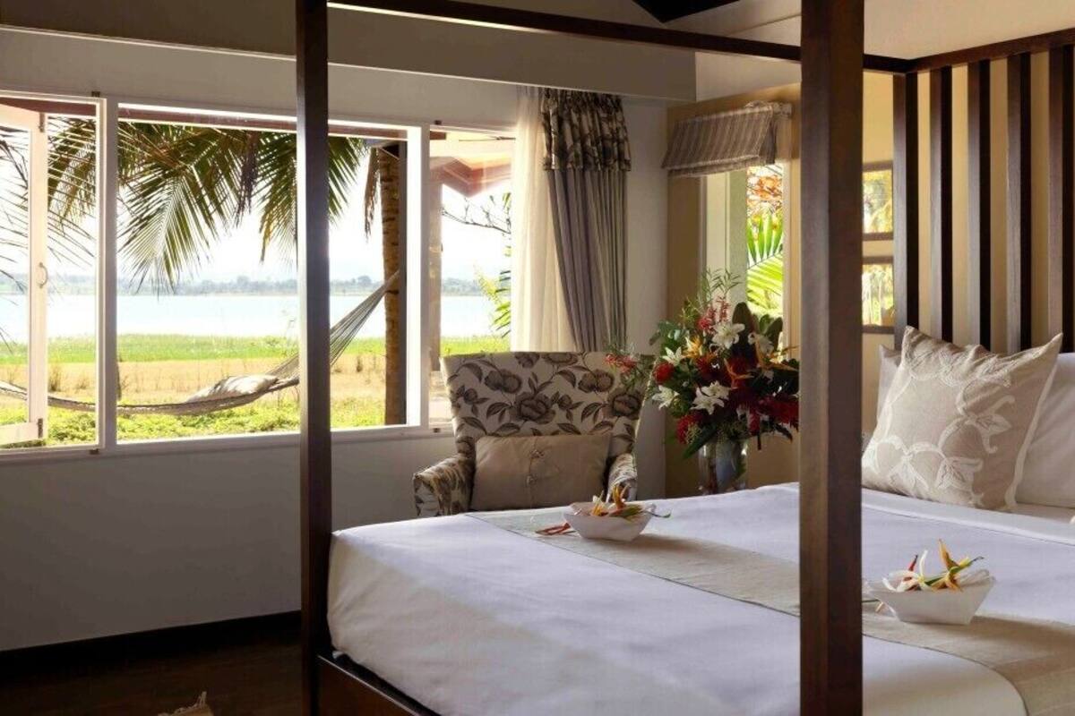 Ein Schlafzimmer mit einem großen Bett, einem Sessel und Blick auf Strand und Palmen.
