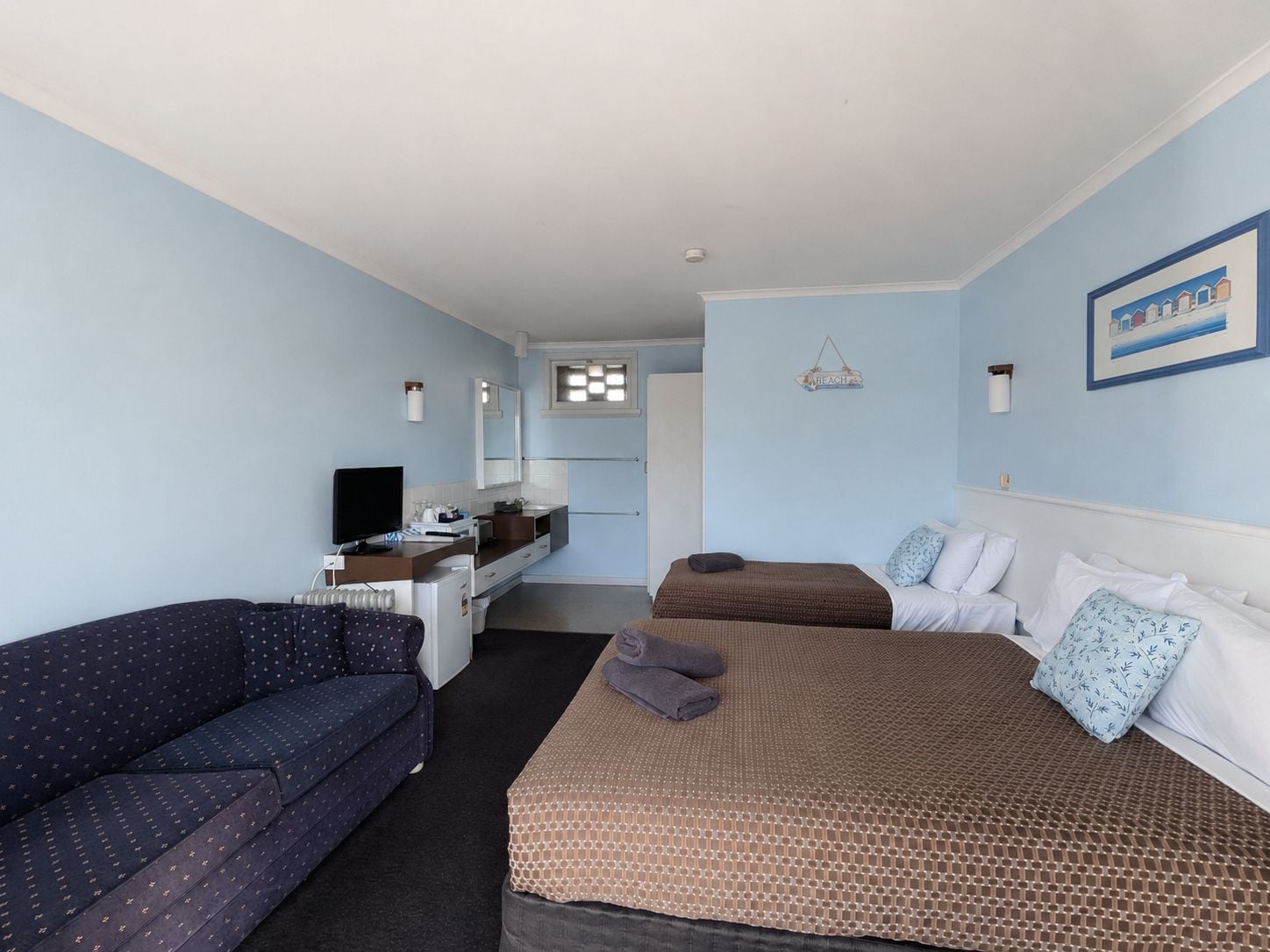 A hotel room with a bed, a sofa, a desk with a TV, and a bathroom in the background.