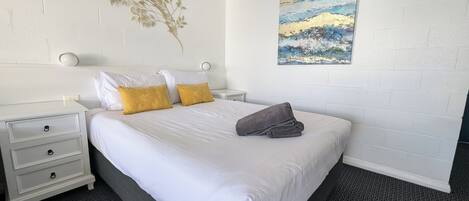 A hotel room with a bed, white nightstands, a wall-mounted lamp, and a painting.