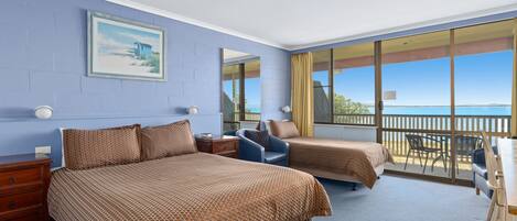 A hotel room with two beds, a desk, and a balcony with a view.