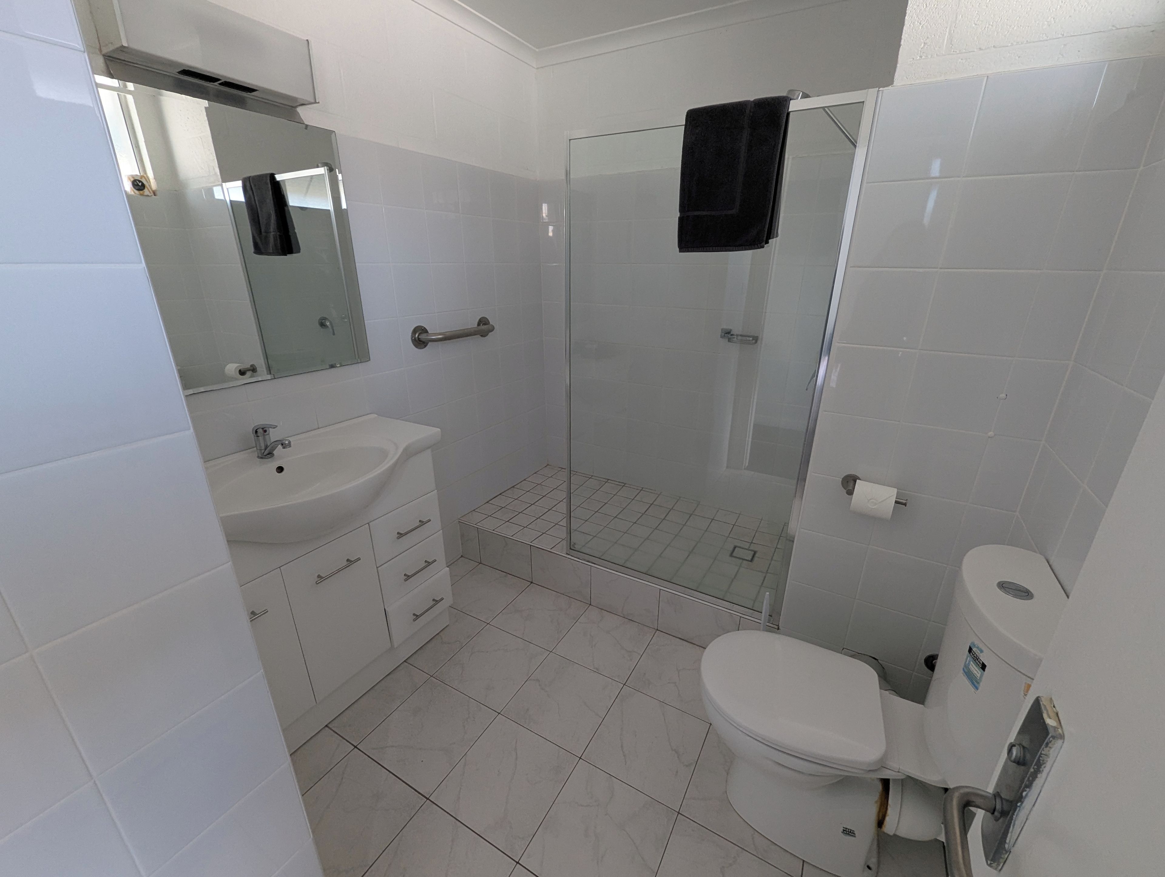 A bathroom with a white sink, mirror, toilet, and a glass shower enclosure.