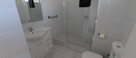 A bathroom with a white sink, mirror, toilet, and a glass shower enclosure.