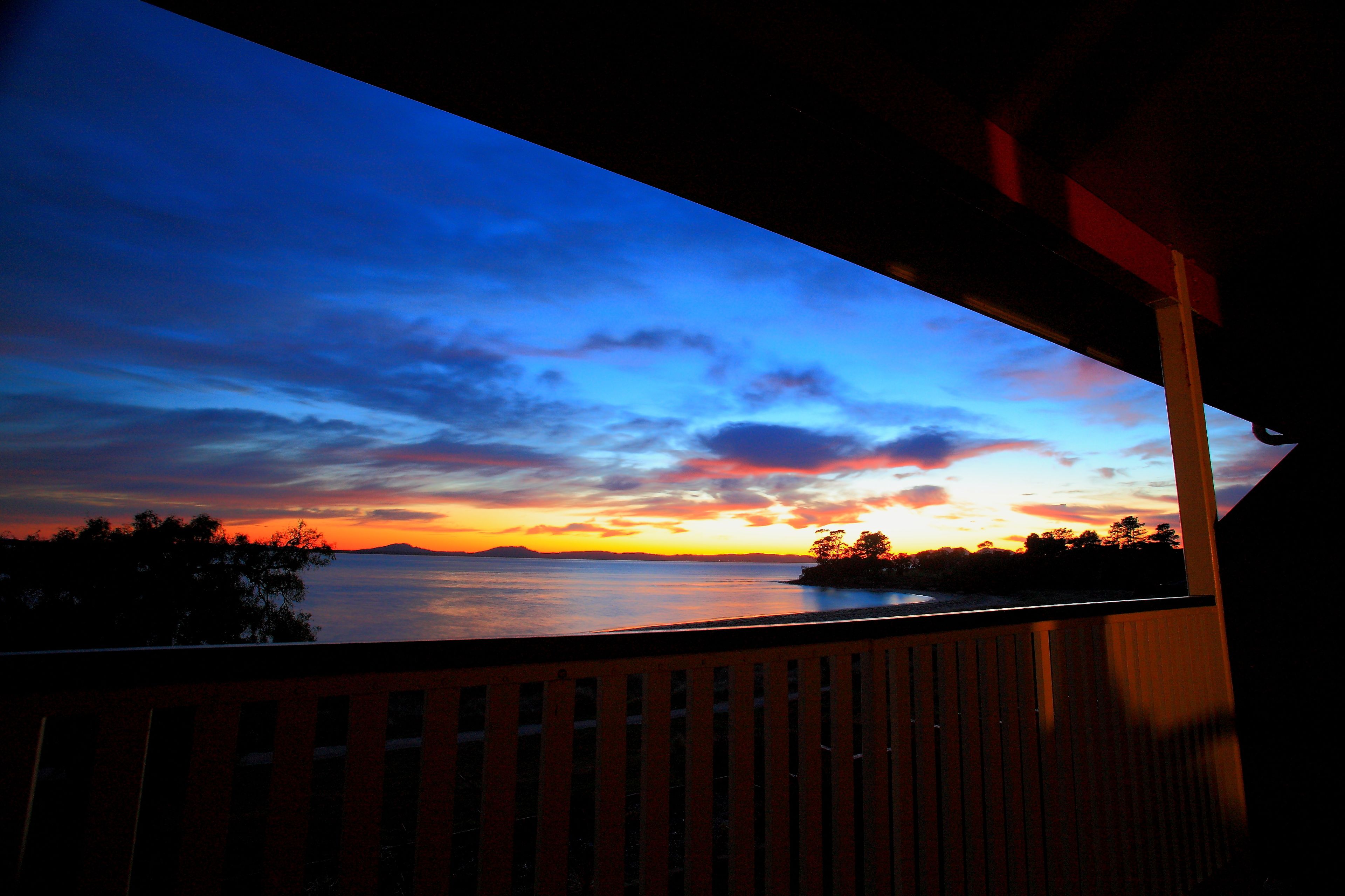 Un balcon donnant sur un coucher de soleil sur une étendue d’eau.