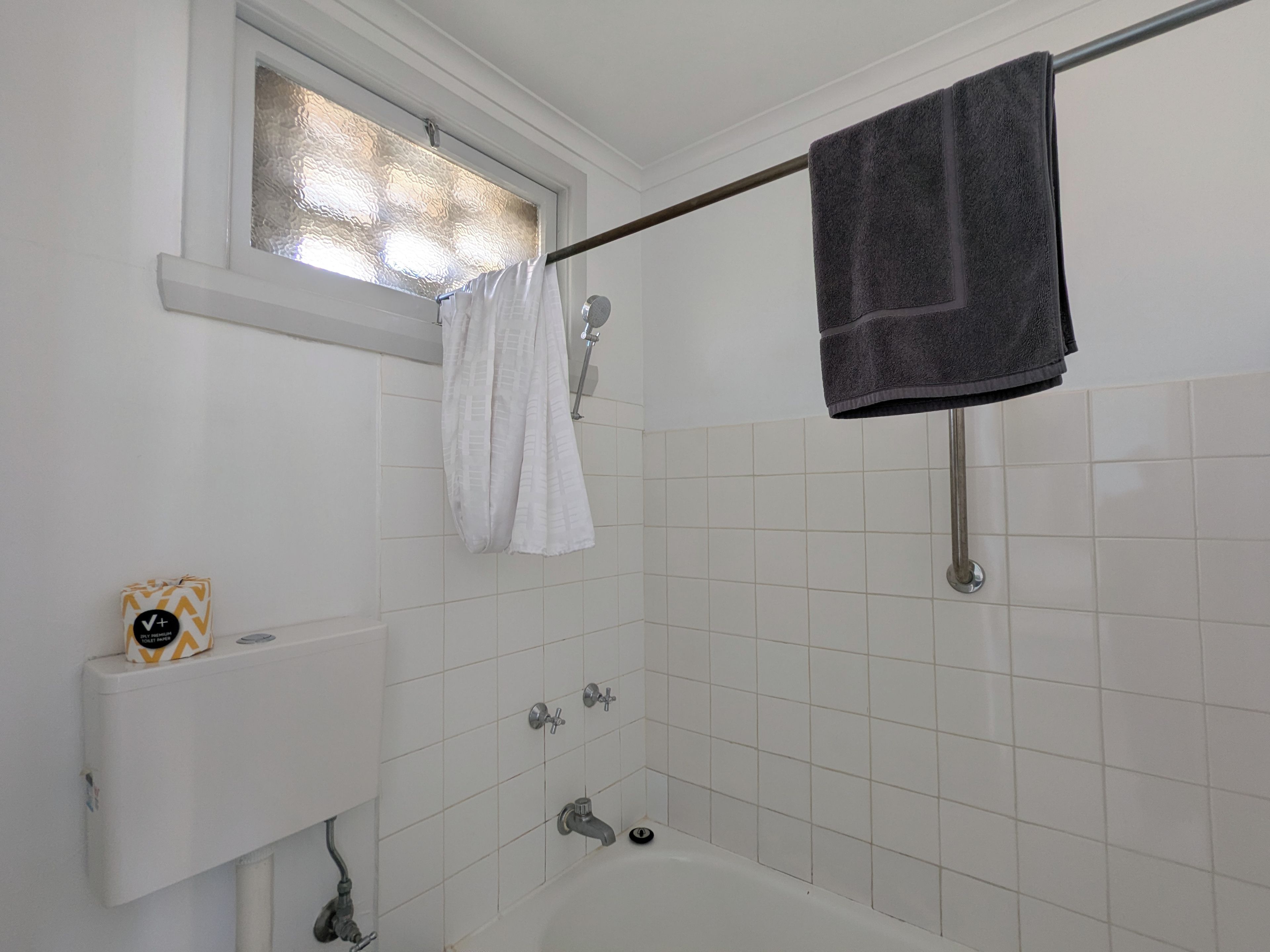 A bathroom with a bathtub, a window with frosted glass, a towel rack with two towels, and a toilet paper holder with a roll.