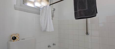 A bathroom with a bathtub, a window with frosted glass, a towel rack with two towels, and a toilet paper holder with a roll.