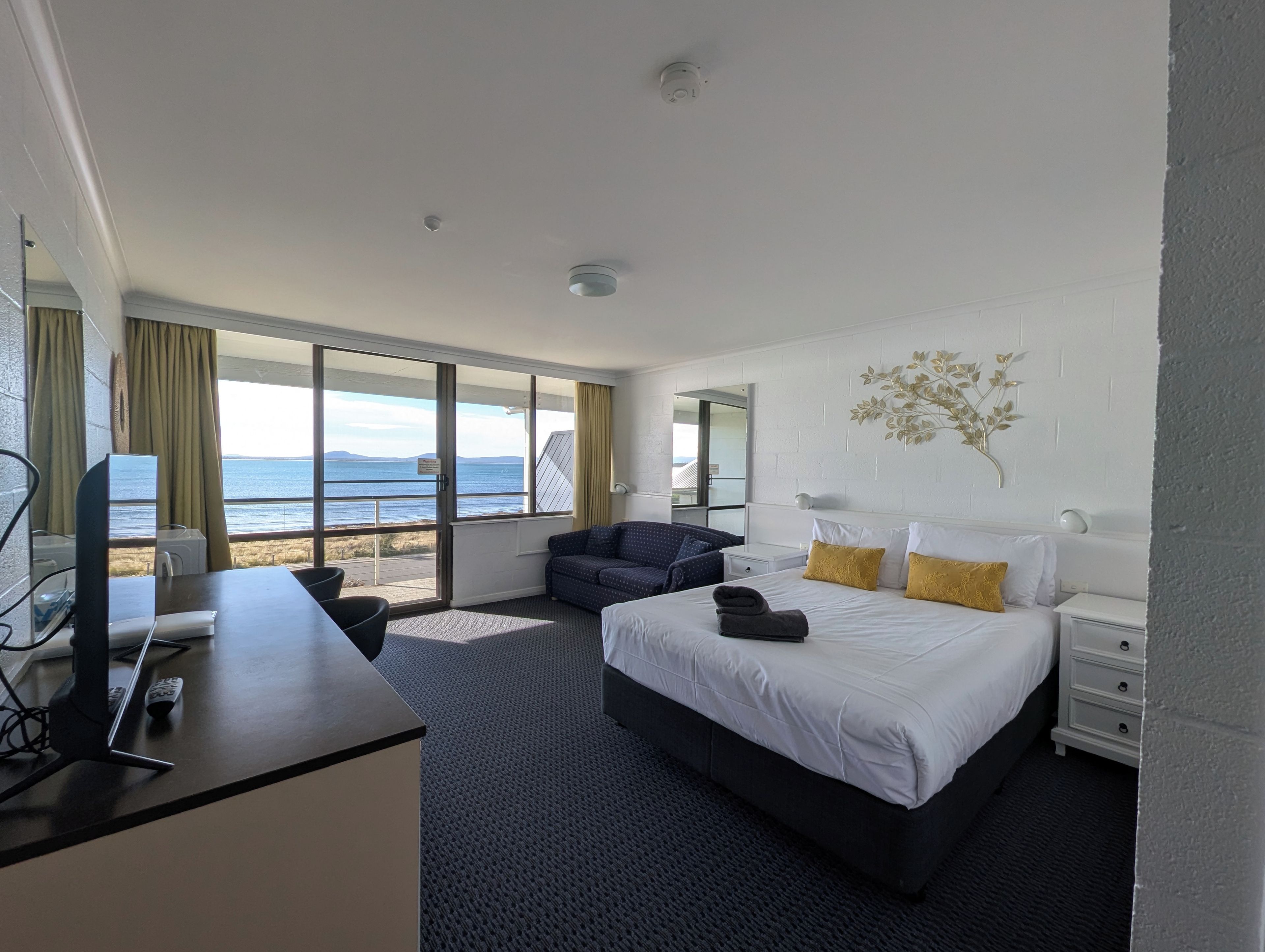 Une chambre d’hôtel avec un lit, un bureau, une chaise, une table de chevet et une vue sur la mer.