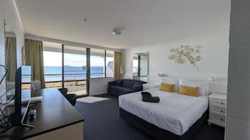 A hotel room with a bed, a desk, a chair, a nightstand, and a view of the sea.