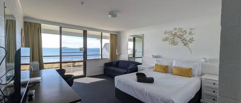 Ein Hotelzimmer mit Bett, Schreibtisch, Stuhl, Nachttisch und Blick auf das Meer.