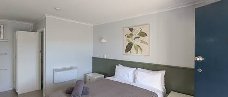Un dormitorio con cama, mesita de noche, cómoda, radiador y puerta.