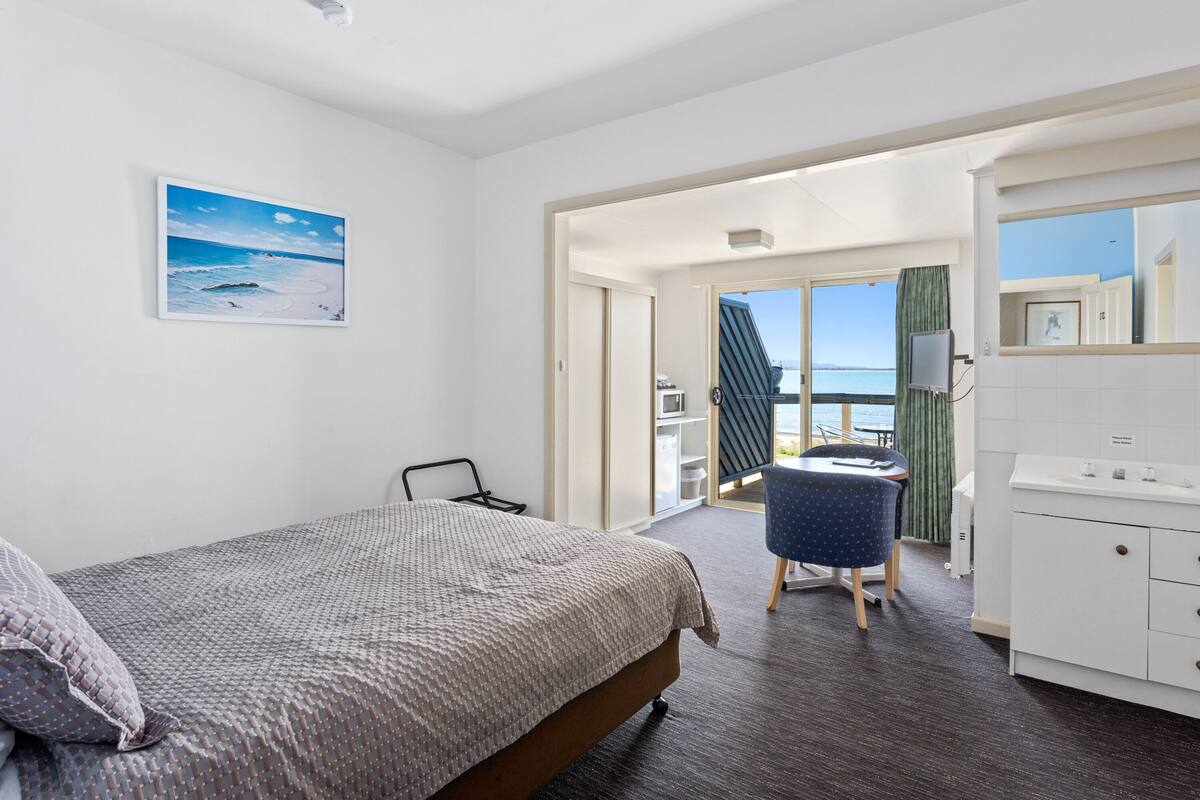 A bedroom with a bed, a desk, and a view of the sea.