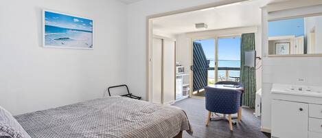 A bedroom with a bed, a desk, and a view of the sea.