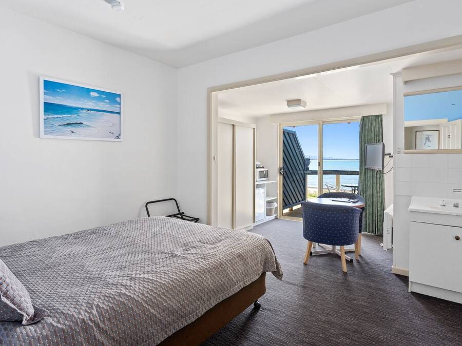 A bedroom with a bed, a desk, and a view of the sea.