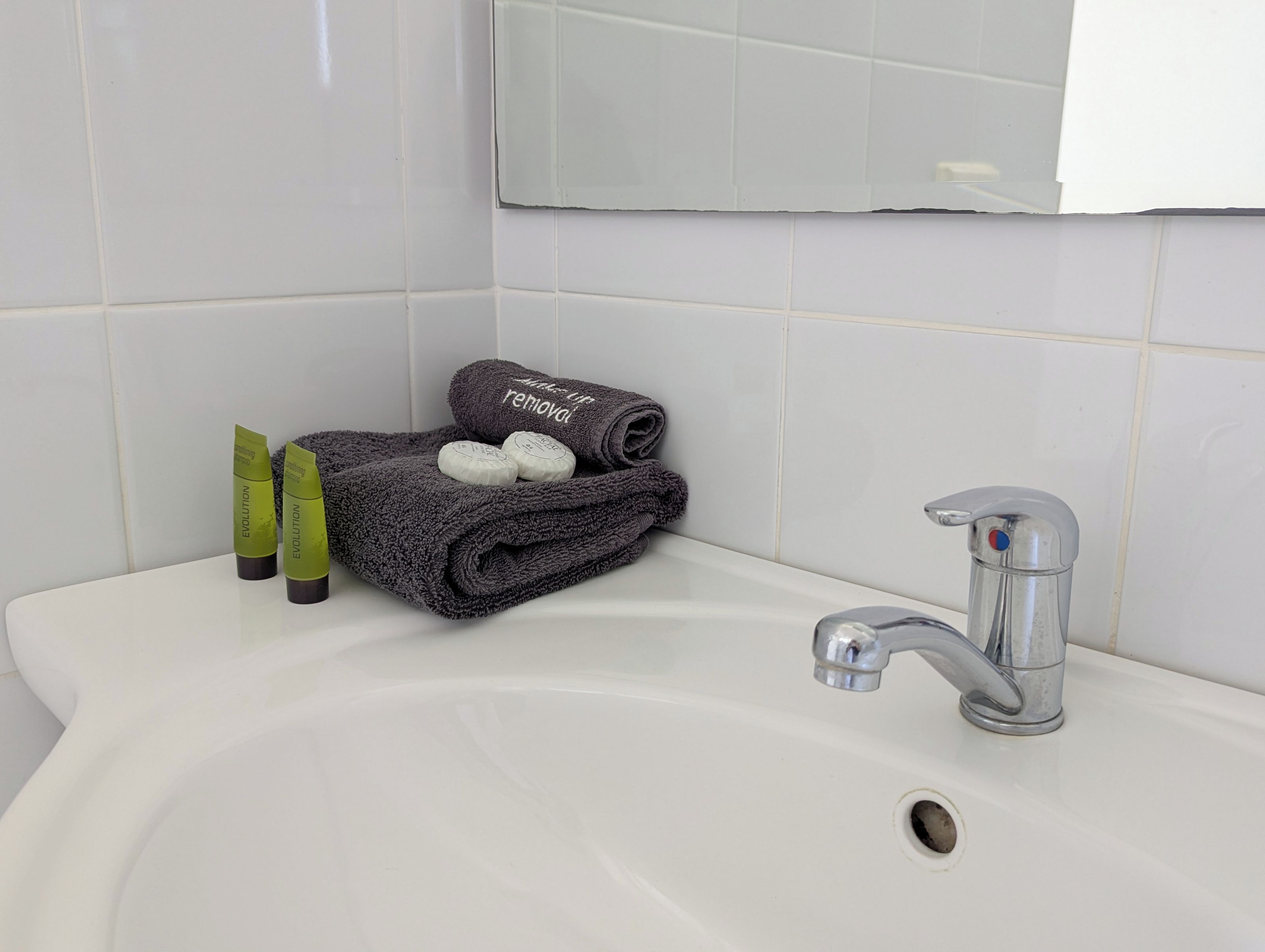 En vask på badeværelset med et spejl, et håndklæde og toiletartikler.