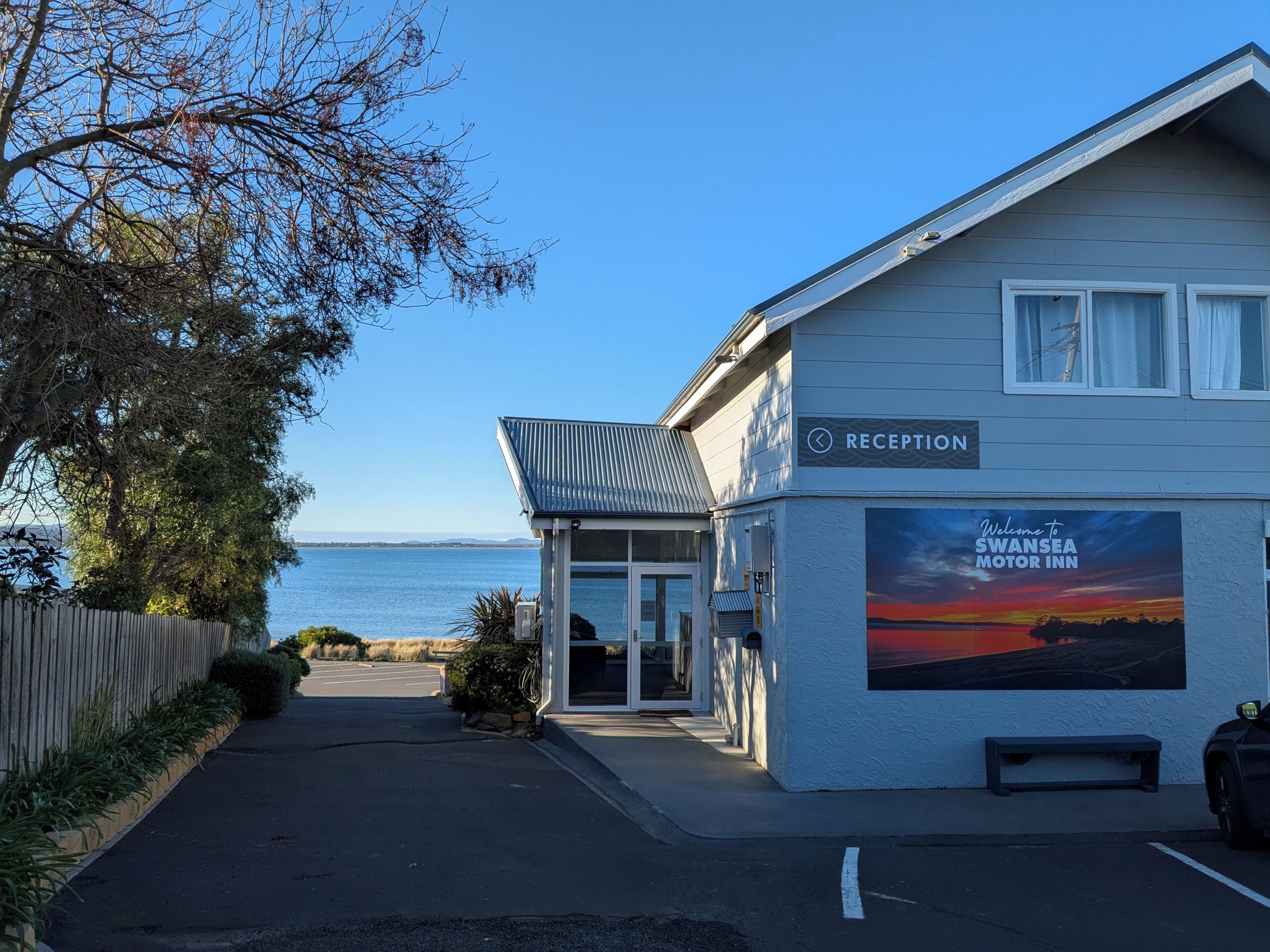 A reception area with a view of the sea, a sign for Swansea Motor Inn, and a bench outside.