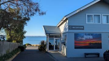 A reception area with a view of the sea, a sign for Swansea Motor Inn, and a bench outside.