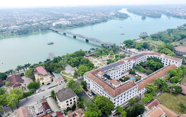An aerial view of a historic building complex with a river and bridge in the background. - Hotel Saigon Morin (Hue)