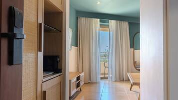 Habitación de hotel con un armario de madera, televisor, ventana con cortinas y vistas al exterior.