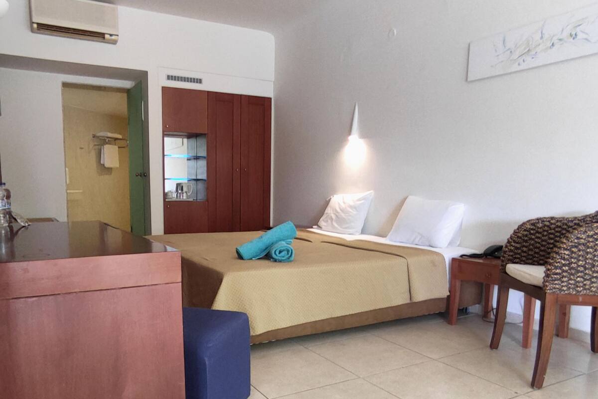 A hotel room with a bed, a desk, a chair, and a kitchenette.