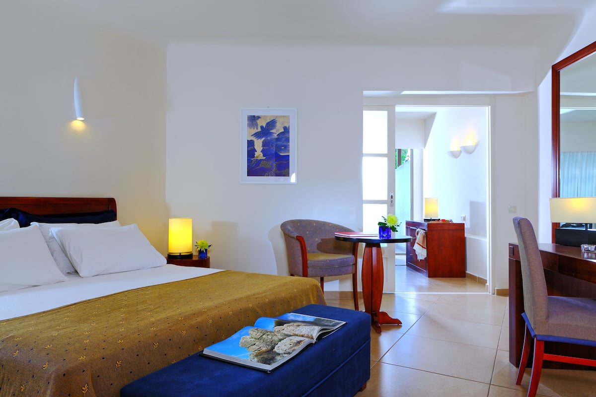 A hotel room with a bed, a desk, a chair, and a small table with a lamp.