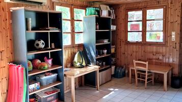 Una habitación con paredes y techo de madera, suelo de baldosas y estantes con diversos objetos, incluyendo balones deportivos, libros y una bolsa verde.